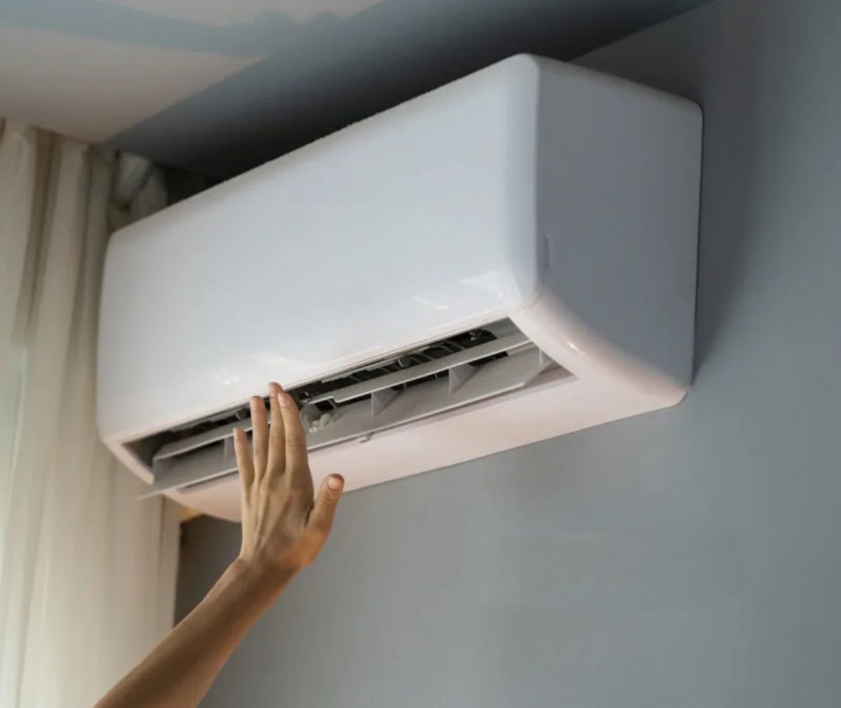 Hand checking the airflow from a wall-mounted air conditioner