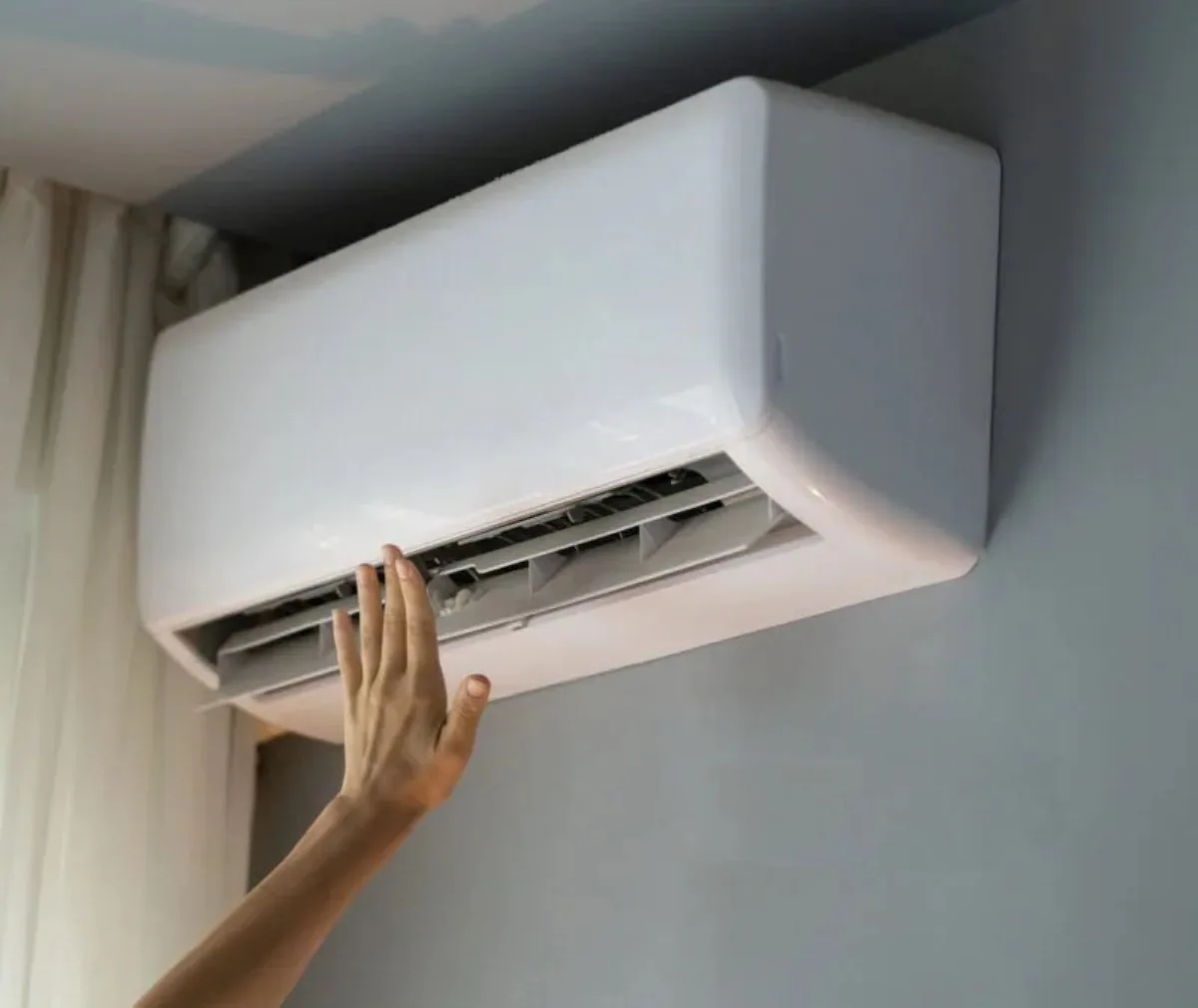 Hand checking the airflow from a wall-mounted air conditioner