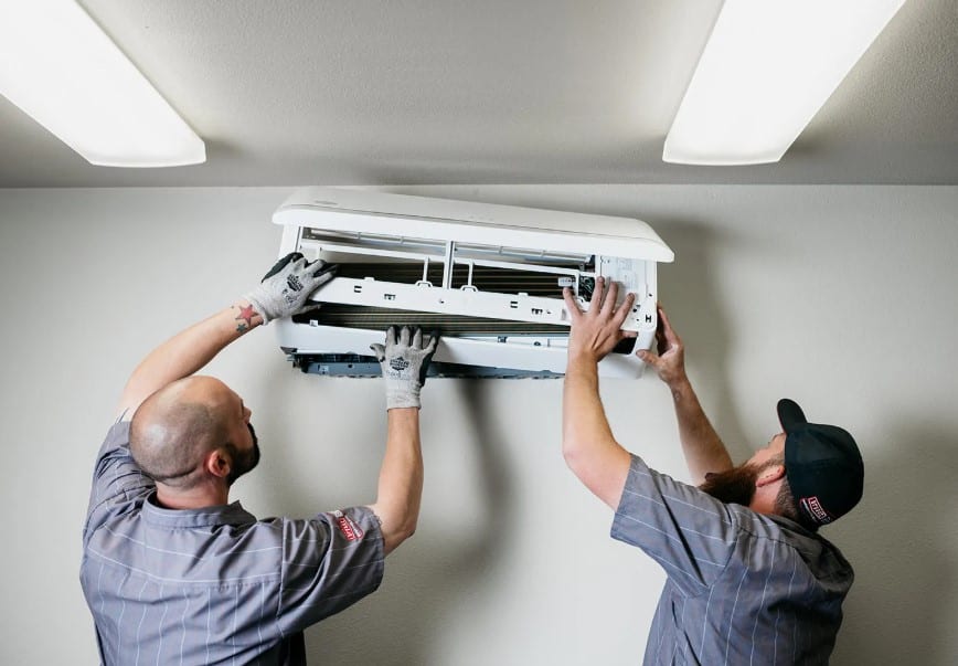 Two HVAC technicians servicing a wall-mounted air conditioner