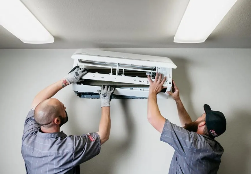 Two HVAC technicians servicing a wall-mounted air conditioner