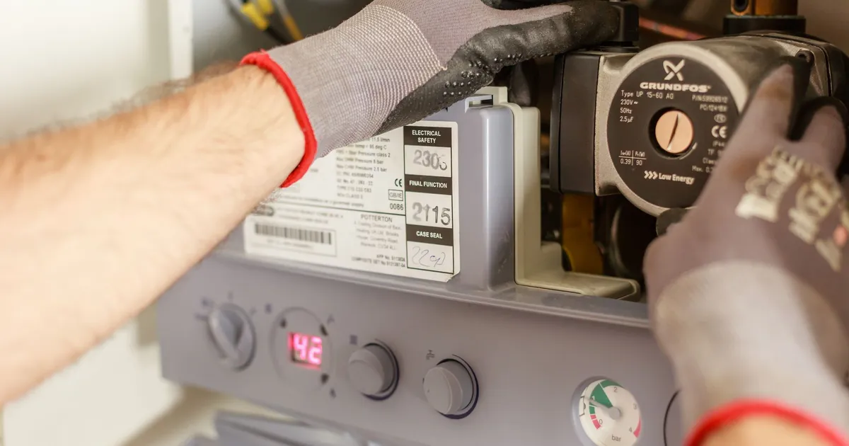 Technician in work gloves checking the circulator pump on a home boiler, with the pressure gauge in view