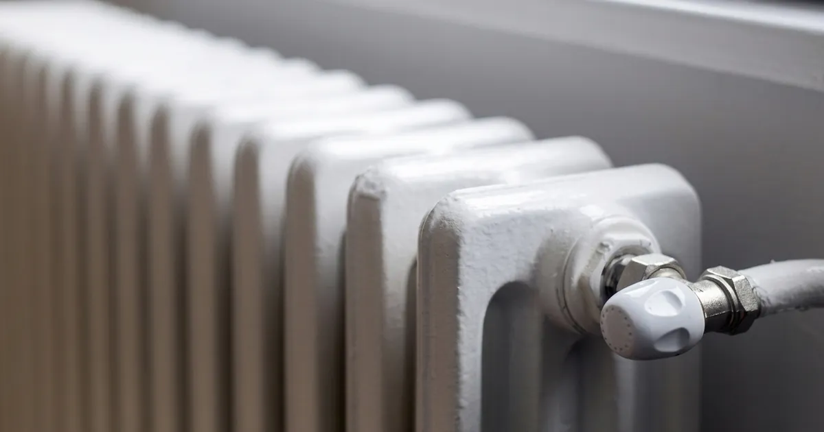 White painted cast iron radiator with a valve on the supply pipe