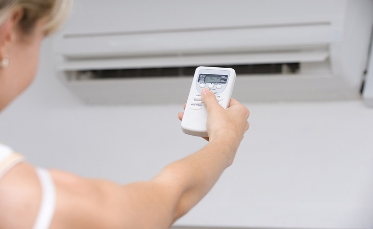 Person adjusting a wall-mounted air conditioner with a handheld remote