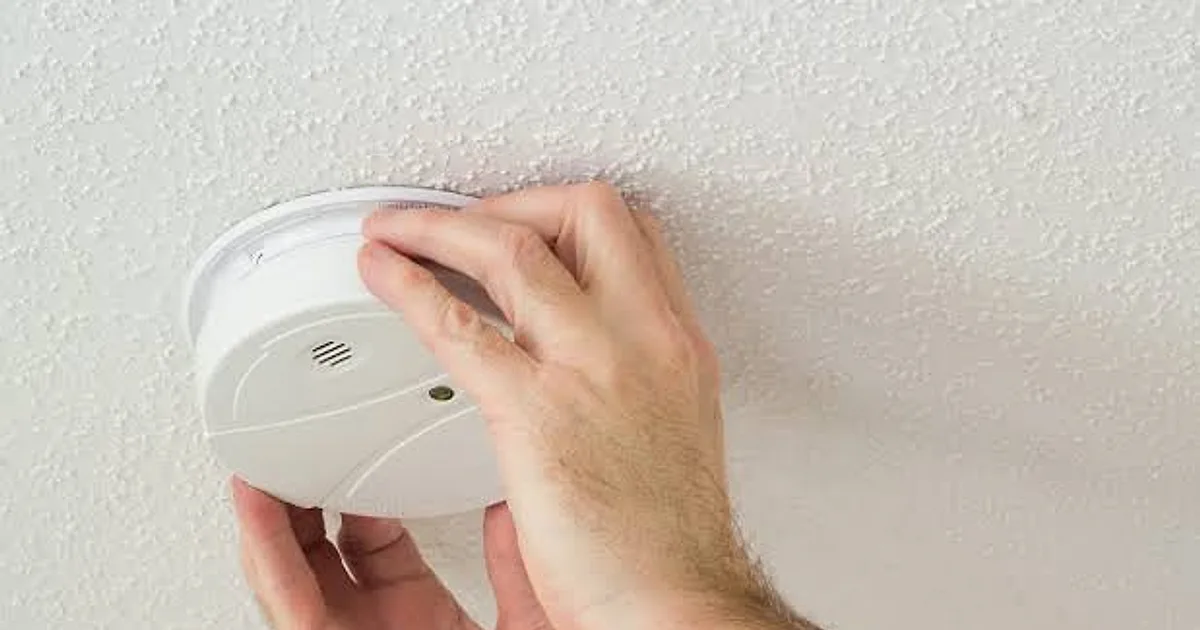 Hands twisting an alarm onto its ceiling mounting plate