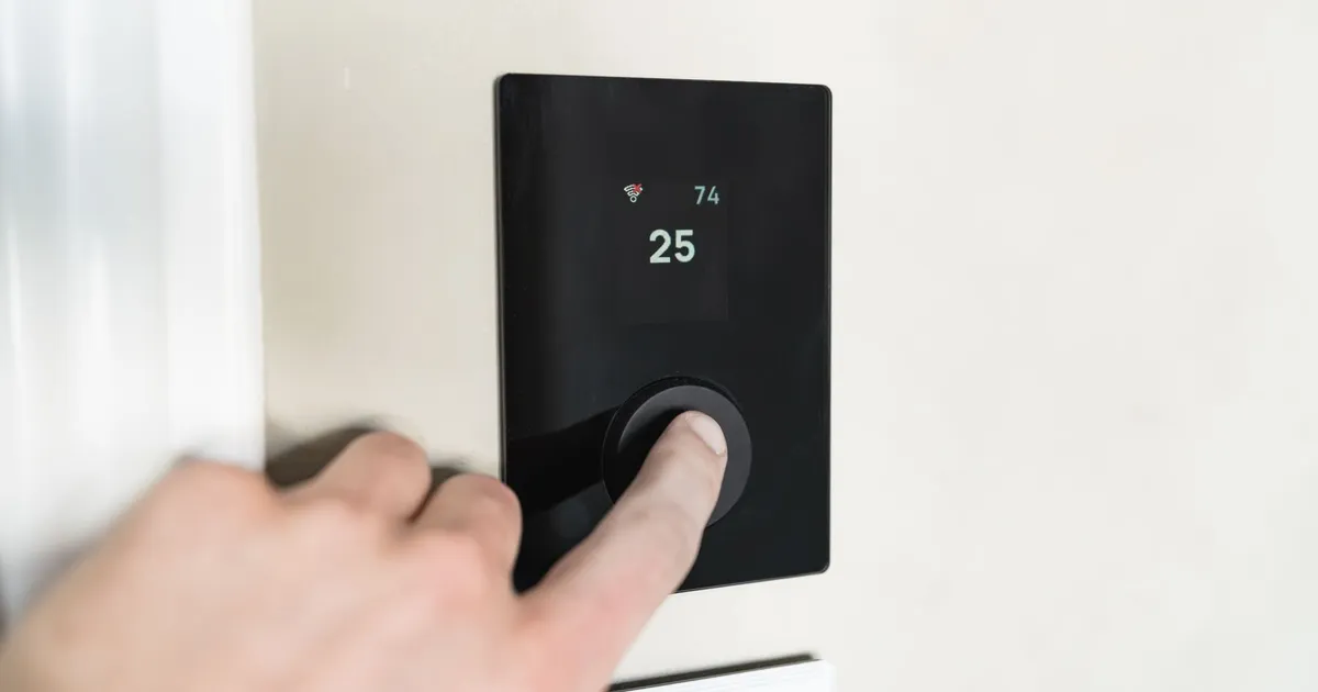 Hand pressing the dial on a wall thermostat