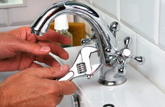 Hands using a wrench to repair a dripping bathroom faucet