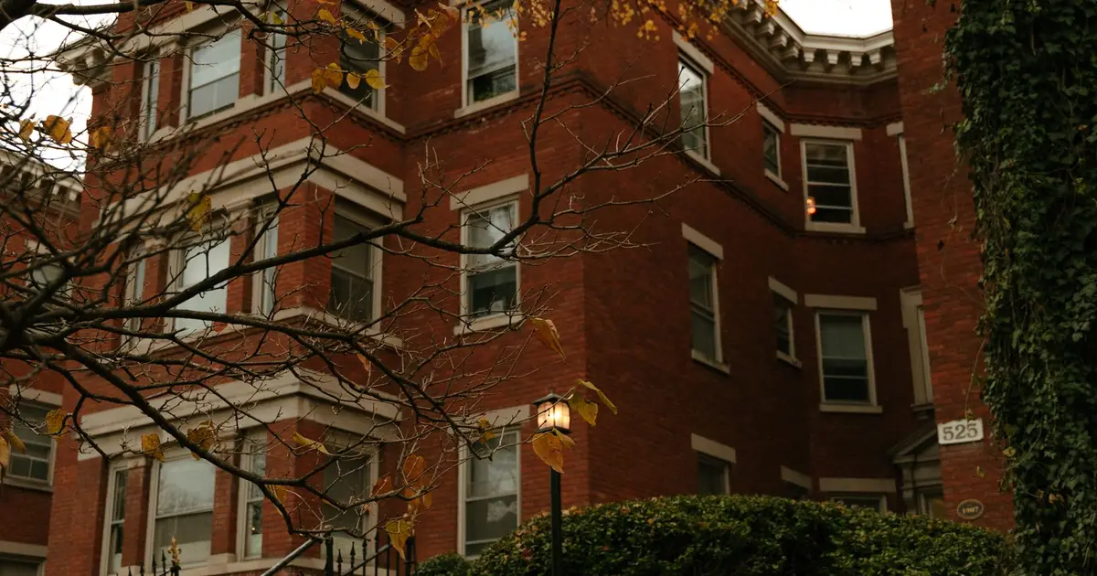 Red brick apartment building with bare branches and a few yellow leaves in late fall