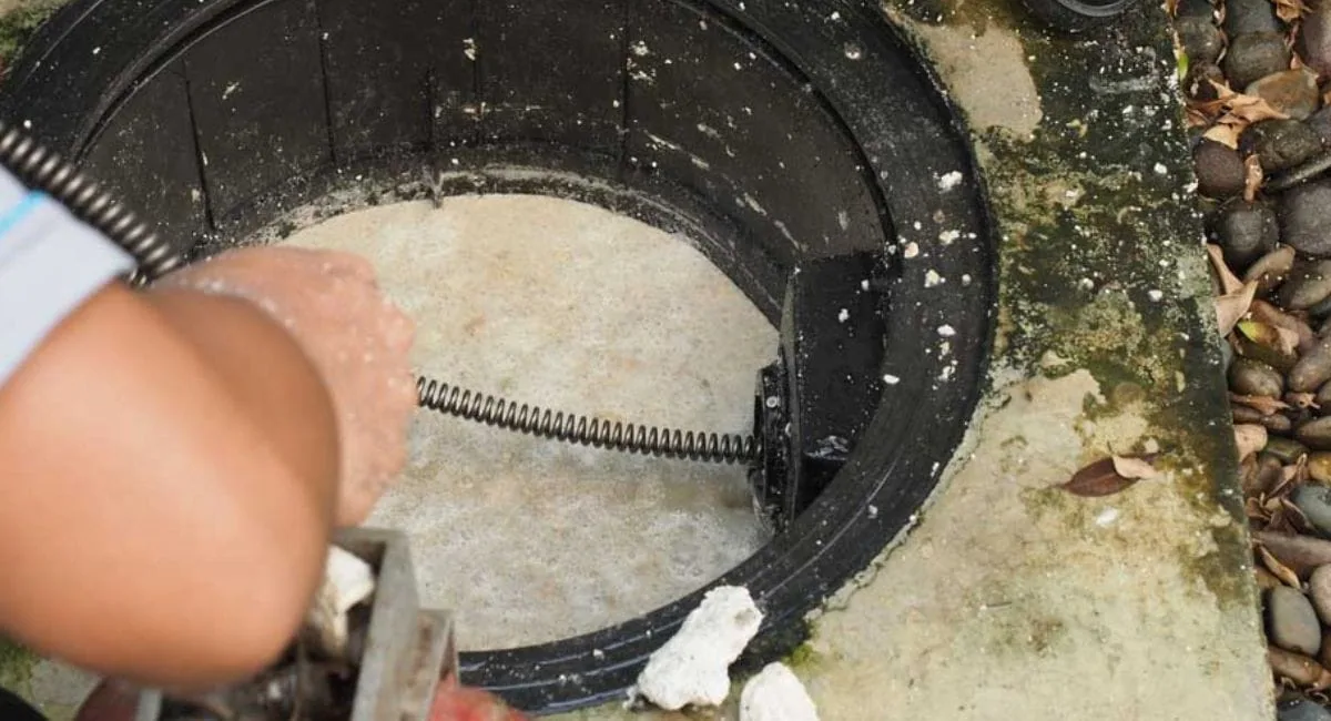 Plumber running a drain snake into an outdoor drain cleanout