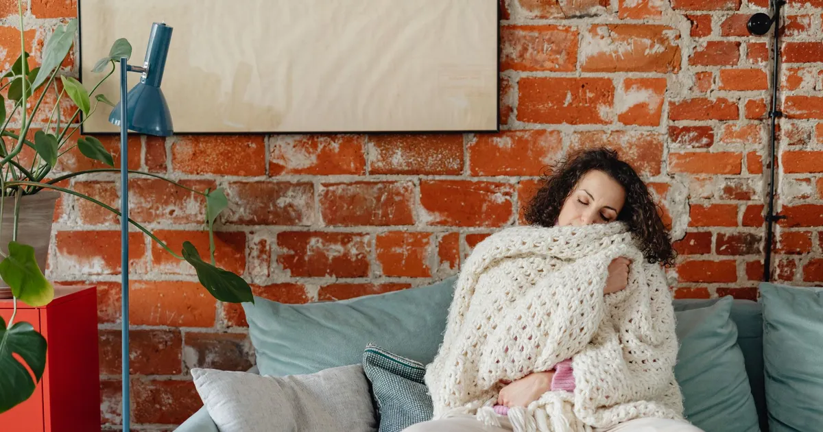 Tenant wrapped in a heavy knit blanket on the couch of a cold apartment