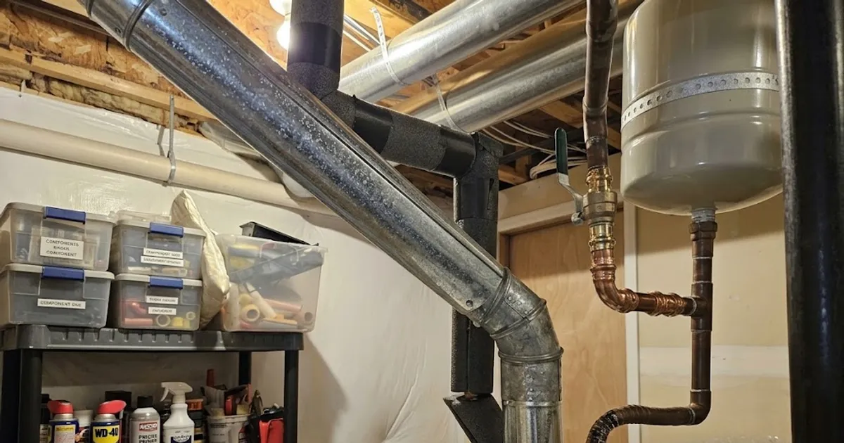 Older home basement with overhead ductwork, a gas water heater vent, and an expansion tank