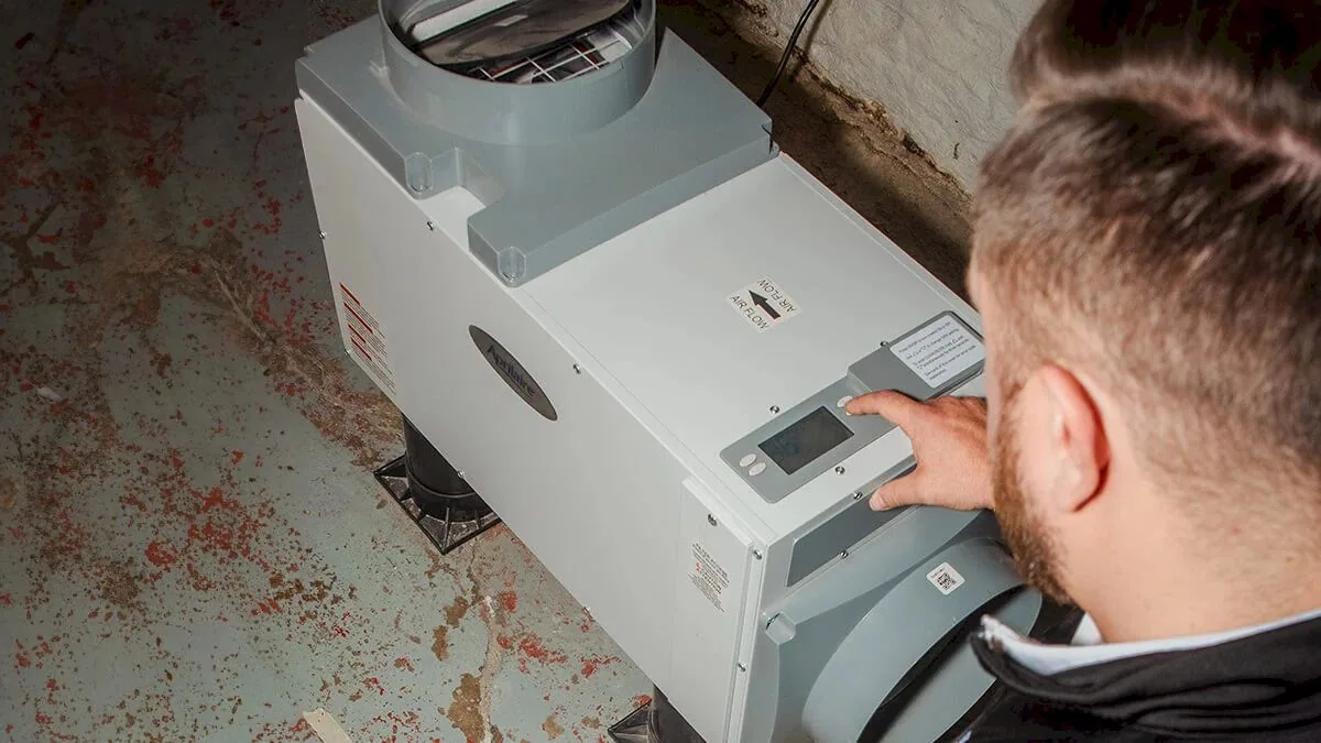 Technician adjusting a whole-home dehumidifier in a basement