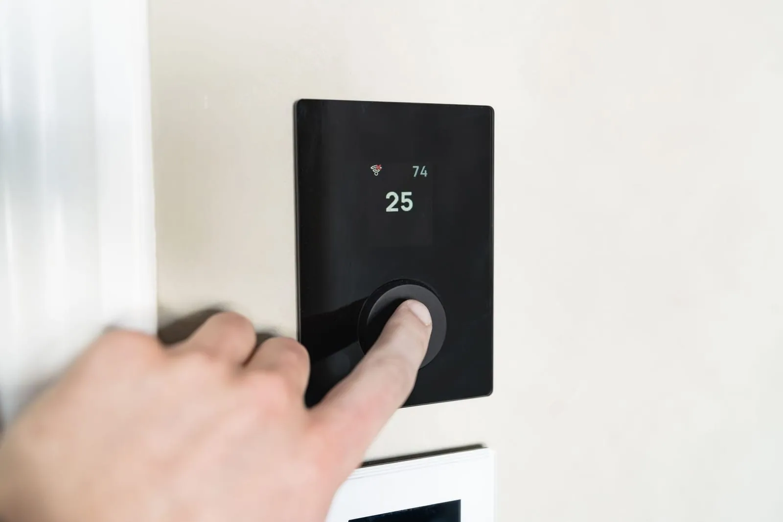 Person adjusting a home thermostat on the wall